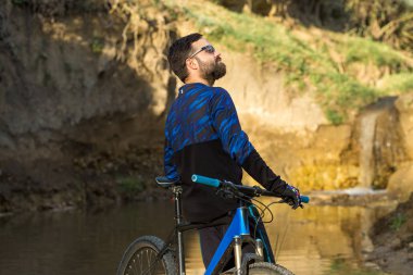 Şort ve mayo modern bir karbon hardtail bisiklet üzerinde bir hava süspansiyon çatal sürmek off-road turuncu-kırmızı tepelerde yaz aylarında gün batımı akşamı