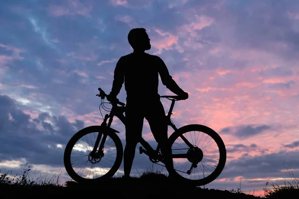 Cyclist in shorts and jersey on a modern carbon hardtail bike with an air suspension fork rides off-road on the orange-red hills at sunset evening in summer