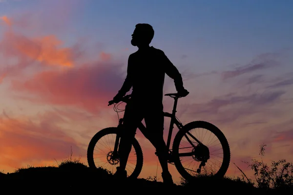 Cyclist in shorts and jersey on a modern carbon hardtail bike with an air suspension fork rides off-road on the orange-red hills at sunset evening in summer