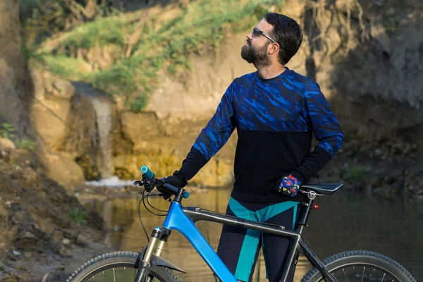 Cyclist in shorts and jersey on a modern carbon hardtail bike with an air suspension fork rides off-road on the orange-red hills at sunset evening in summer