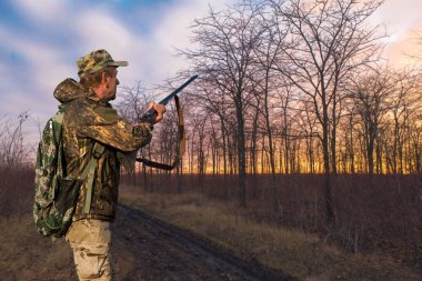 Silahlı bir avcı ve bir köpek bozkırda ilk kara çıkarlar yansıtıcı yelek giymiş sülün avlarlar.