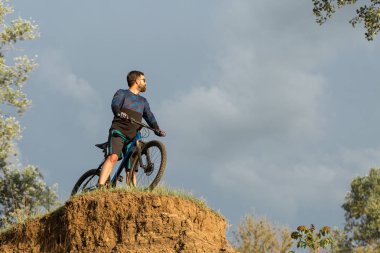 Şort ve mayo modern bir karbon hardtail bisiklet üzerinde bir hava süspansiyon çatal sürmek off-road turuncu-kırmızı tepelerde yaz aylarında gün batımı akşamı