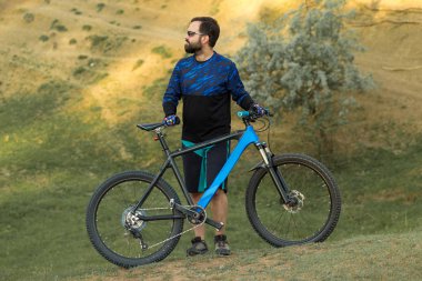 Şort ve mayo modern bir karbon hardtail bisiklet üzerinde bir hava süspansiyon çatal sürmek off-road turuncu-kırmızı tepelerde yaz aylarında gün batımı akşamı
