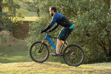 Şort ve mayo modern bir karbon hardtail bisiklet üzerinde bir hava süspansiyon çatal sürmek off-road turuncu-kırmızı tepelerde yaz aylarında gün batımı akşamı