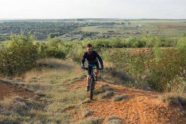 Şort ve mayo modern bir karbon hardtail bisiklet üzerinde bir hava süspansiyon çatal sürmek off-road turuncu-kırmızı tepelerde yaz aylarında gün batımı akşamı