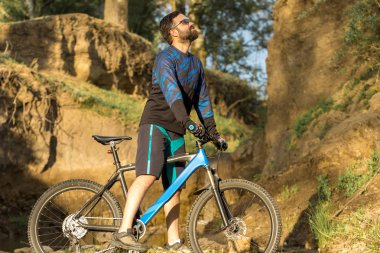 Şort ve mayo modern bir karbon hardtail bisiklet üzerinde bir hava süspansiyon çatal sürmek off-road turuncu-kırmızı tepelerde yaz aylarında gün batımı akşamı