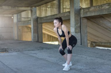 İnce atletik kız bitmemiş bir binanın çatısında germe egzersizleri gerçekleştirir, kentsel arka plan.