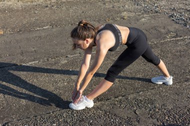 İnce atletik kız bitmemiş bir binanın çatısında germe egzersizleri gerçekleştirir, kentsel arka plan.