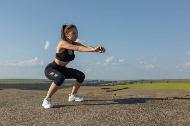 İnce atletik kız bitmemiş bir binanın çatısında germe egzersizleri gerçekleştirir, kentsel arka plan.