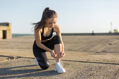 İnce atletik kız bitmemiş bir binanın çatısında germe egzersizleri gerçekleştirir, kentsel arka plan.