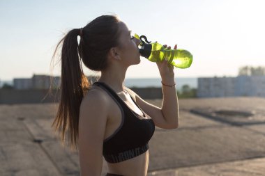 İnce atletik kız bitmemiş bir binanın çatısında germe egzersizleri gerçekleştirir, kentsel arka plan.