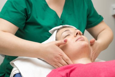 Genç bir kadın güzellik salonunda yüz masajı yaptırıyor.