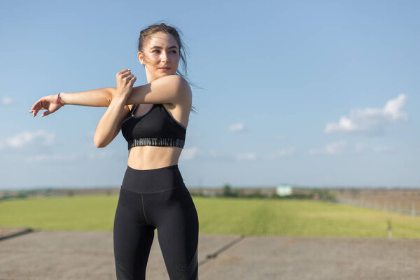 Slim athletic girl performs stretching exercises on the roof of an unfinished building, urban background.