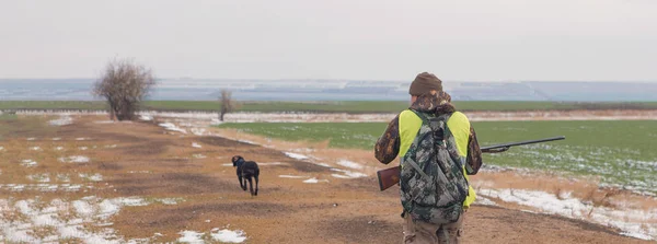 Hunter with a gun and a dog go on the first snow in the steppe, Hunting pheasant in a reflective vest