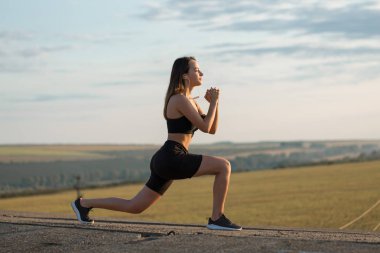 İnce atletik kız bitmemiş bir binanın çatısında germe egzersizleri gerçekleştirir, kentsel arka plan.
