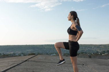 İnce atletik kız bitmemiş bir binanın çatısında germe egzersizleri gerçekleştirir, kentsel arka plan.