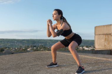 İnce atletik kız bitmemiş bir binanın çatısında germe egzersizleri gerçekleştirir, kentsel arka plan.