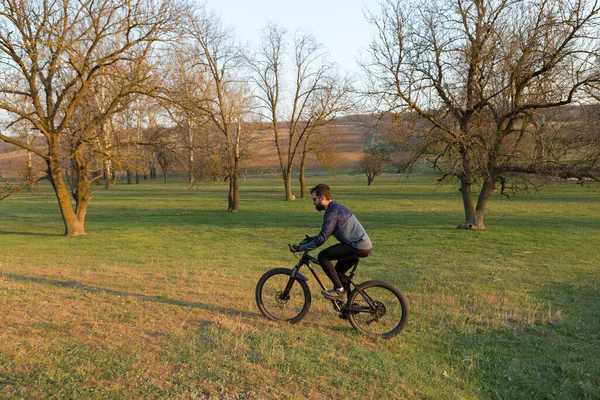 Cyclist in shorts and jersey on a modern carbon hardtail bike with an air suspension fork standing on a cliff against the background of fresh green spring forest