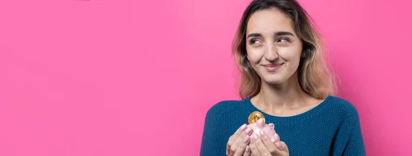 女孩把身体上的比特币放进储蓄罐 粉红背景的女孩拿着储蓄罐 高兴地做着手势 现金投资和保险可靠性的概念 — 图库照片