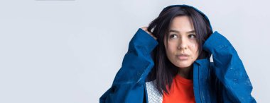 Mavi yağmurluk giymiş gülümseyen bir kızın portresi. Stüdyoda gri arka planda kapüşonlu poz veren bir kız..