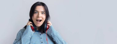 Çizgili yelek giymiş genç bir kız stüdyoda kırmızı kulaklıkla müzik dinliyor ve dans ediyor..