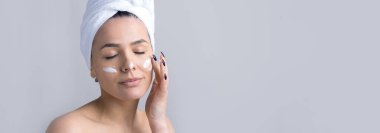 Kafasında beyaz havlu olan bir kadının güzel portresi yüzüne krem sürüyor. Cilt temizleme eko organik kozmetik rahatlama konsepti.