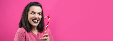 Güzel, güzel, neşeli, düz kahverengi saçlı bir kadının portresi. Kırmızı şeker kamışı Noel 'ini ısırmaya çalışıyor..