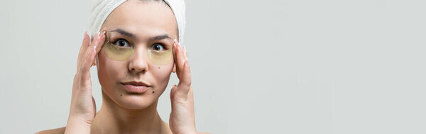 Молодая красивая девушка в белом полотенце на голове носит коллагеновые гелевые пятна под глазами. Маска под глазами
.
