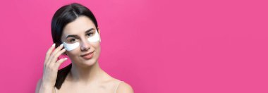 Çıplak omuzlu, göz altı yamalı oldukça çekici bir kızın portresi. Pembe arka planda duruyor.