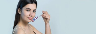 Açık renk bluzlu, beyaz arka planda yüz makyajı yapan genç bir kızın yakın çekimi. Güzel bir kadın yüzüne bir makyaj fırçası tutar ve gülümser..