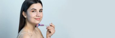 Açık renk bluzlu, beyaz arka planda yüz makyajı yapan genç bir kızın yakın çekimi. Güzel bir kadın yüzüne bir makyaj fırçası tutar ve gülümser..