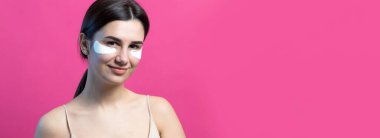 Çıplak omuzlu, göz altı yamalı oldukça çekici bir kızın portresi. Pembe arka planda duruyor.