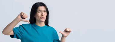 Mavi kolsuz tişörtlü genç bir esmer, olumsuz bir ifadeyle başparmak hareketi yapıyor.