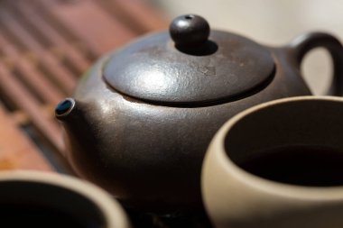Çin çay seremonisi. Balçıktan yapılmış seramik çaydanlık ve ahşap bir arka planda kaseler.