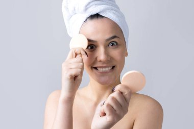 Kafasında beyaz havluyla güzel bir kadın portresi ve pembe bir kalbe bakan bir vücut için sünger. Cilt temizleme eko organik kozmetik rahatlama konsepti.