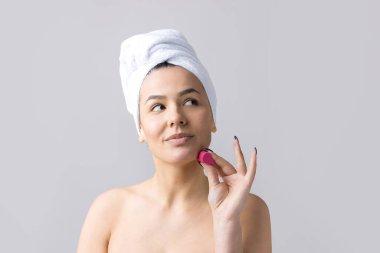 Kafasında beyaz havluyla güzel bir kadın portresi ve pembe bir kalbe bakan bir vücut için sünger. Cilt temizleme eko organik kozmetik rahatlama konsepti.