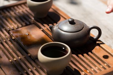 Çin çay seremonisi. Balçıktan yapılmış seramik çaydanlık ve ahşap bir arka planda kaseler.