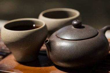 Çin çay seremonisi. Balçıktan yapılmış seramik çaydanlık ve ahşap bir arka planda kaseler.