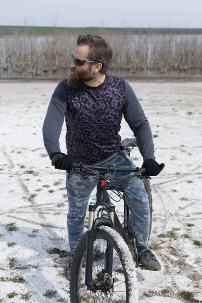 Sports brutal bearded guy on a modern mountain bike. A cyclist in a salt deserted place by the lake.