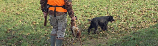 在多云的天气里 一个拿着枪 穿着橙色背心在森林里猎杀野鸡的男人 一个手里拿着野鸡的猎人 — 图库照片