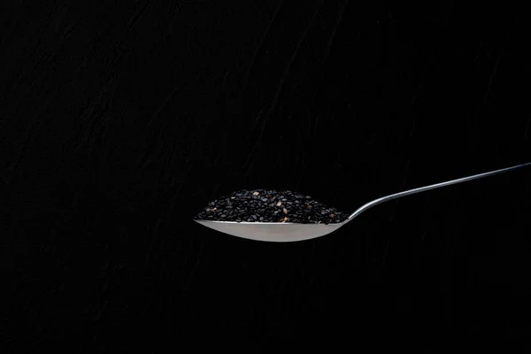 Isolated spoon full of sesame seeds in a black background