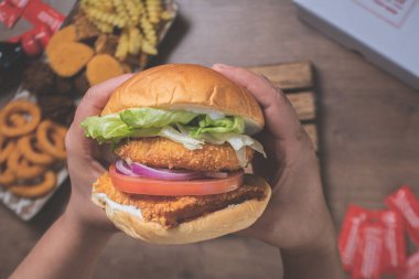 Masanın üzerinde birkaç porsiyon kızarmış atıştırmalık bulunan el yapımı bir burger yiyen birinin bakış açısı.