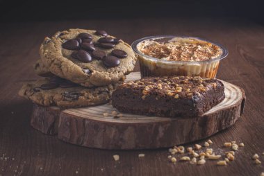 Bir porsiyon taze kurabiye, çikolatalı brownie fındıklı ve banaffee turtası izole bir tahtanın üstünde..