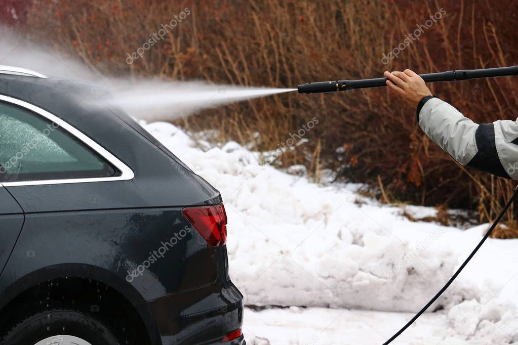 A man washes the dirt and salt off his car in winter. 