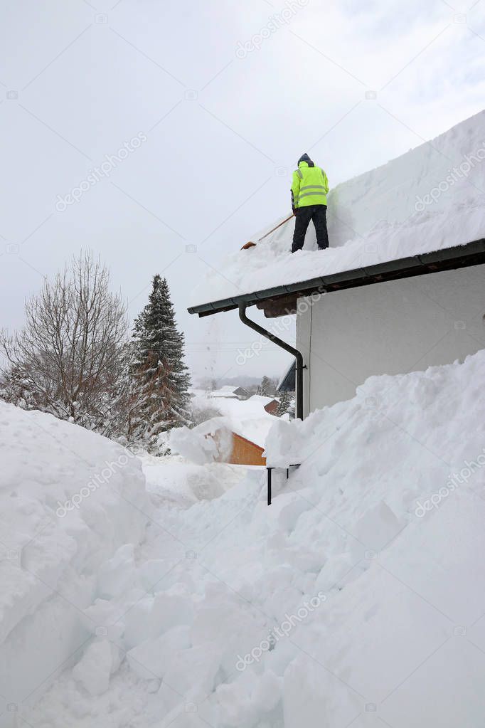 A man shoveling high, heavy snow from a house roof