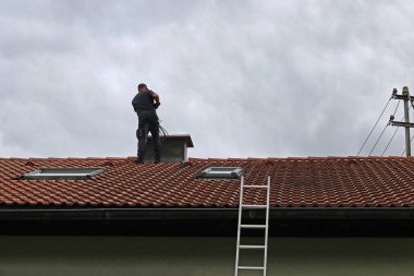 Çatıdaki baca temizleyicisi fırçayla bacayı temizliyor..