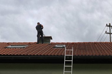 A chimney sweeper on the roof cleans a chimney with a brush. clipart
