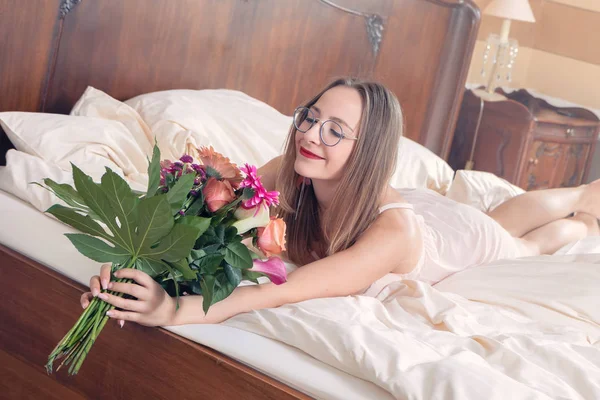 Jonge vrouw met een boeket bloemen in bed — Stockfoto