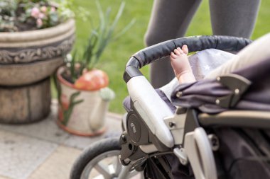 Yalınayak çocuk bacağından rahat bebek arabası... Bebek arabası içinde açık havada yürüyüş sırasında oturan çocuk. Sportif anne arka plan üzerinde. Parlak yaz gün