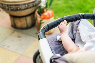 Yalınayak çocuk bacağından rahat bebek arabası... Bebek arabası içinde açık havada yürüyüş sırasında oturan çocuk. Parlak yaz gün